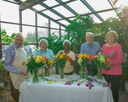 a group of seniors in front of a table of flowers in vases.